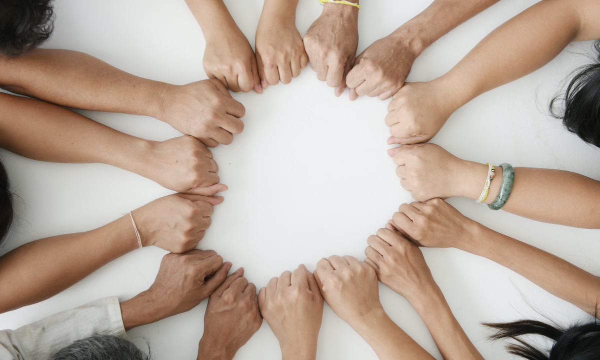 Photo of arms resting on a table joining in a circle, signifying cooperation